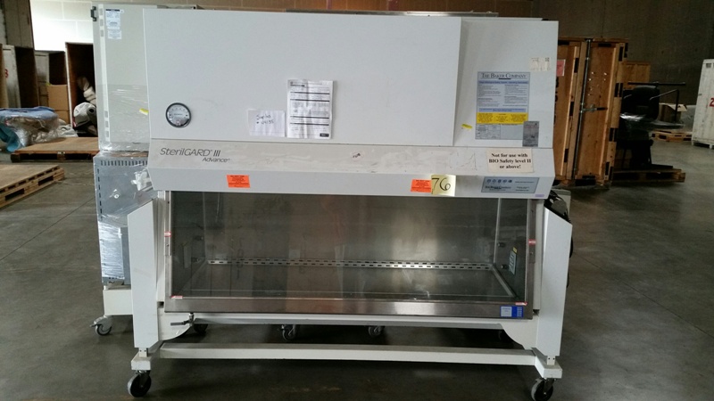 A large laboratory biosafety cabinet on wheels, featuring a transparent front and control panel, set in a warehouse environment.