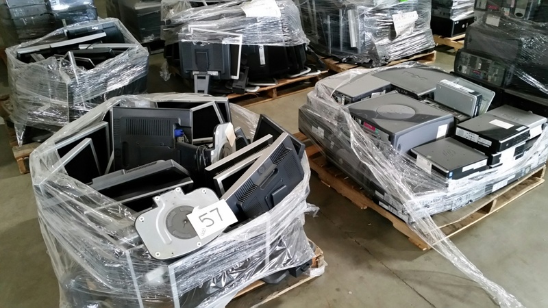Pallets of wrapped electronic equipment, including monitors and other devices, stacked in a warehouse.
