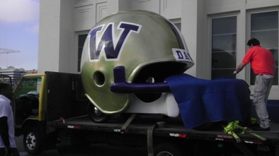 A large, decorative football helmet with a "W" logo is being unloaded from a truck, covered with a blue cloth.
