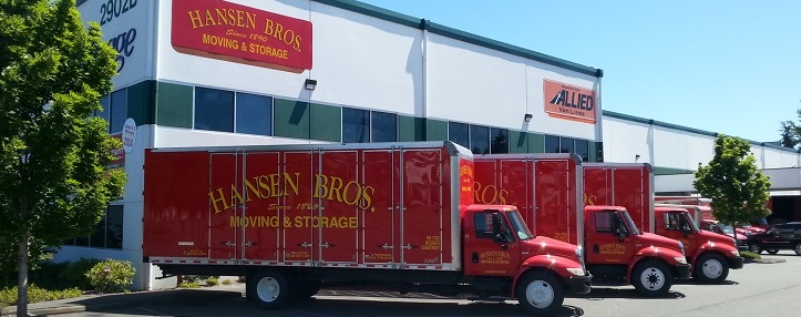 Red Hansen Bros. Moving & Storage trucks parked outside their commercial moving and storage facility, with the company logo visible on the building and trucks.